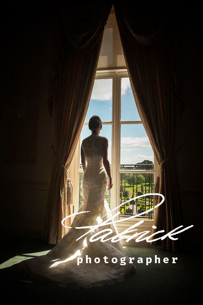 Luton Hoo bride looking out of window into gardens. silhouette lightly lit from behind. sky blue and clouds