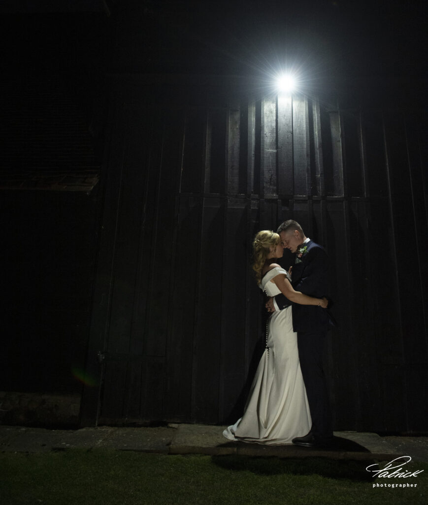 bride and groom illuminated in front of barn doors at night