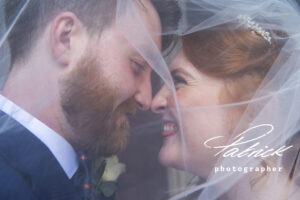 bride, red hair, ginger hair, hair pinned up, groom, beard, under veil, close up, pulling happy funny faces, face to face