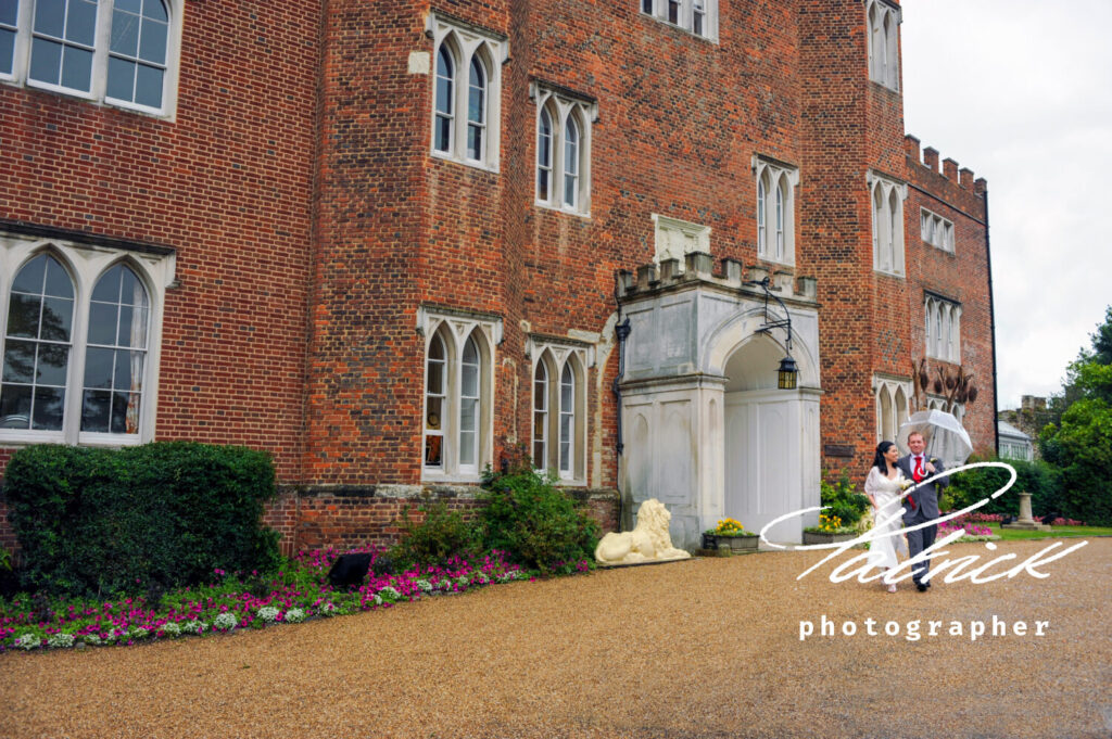 hertford castle exterior taken from side angle, bride and groom walk with transparent umbrella