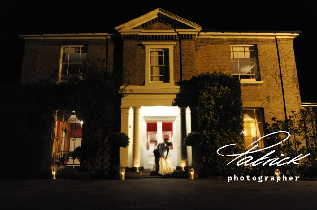 night shot Georgian manor house fennes bride and groom in doorway, red interior walls, low lighting, soft focus, candles on the driveway.