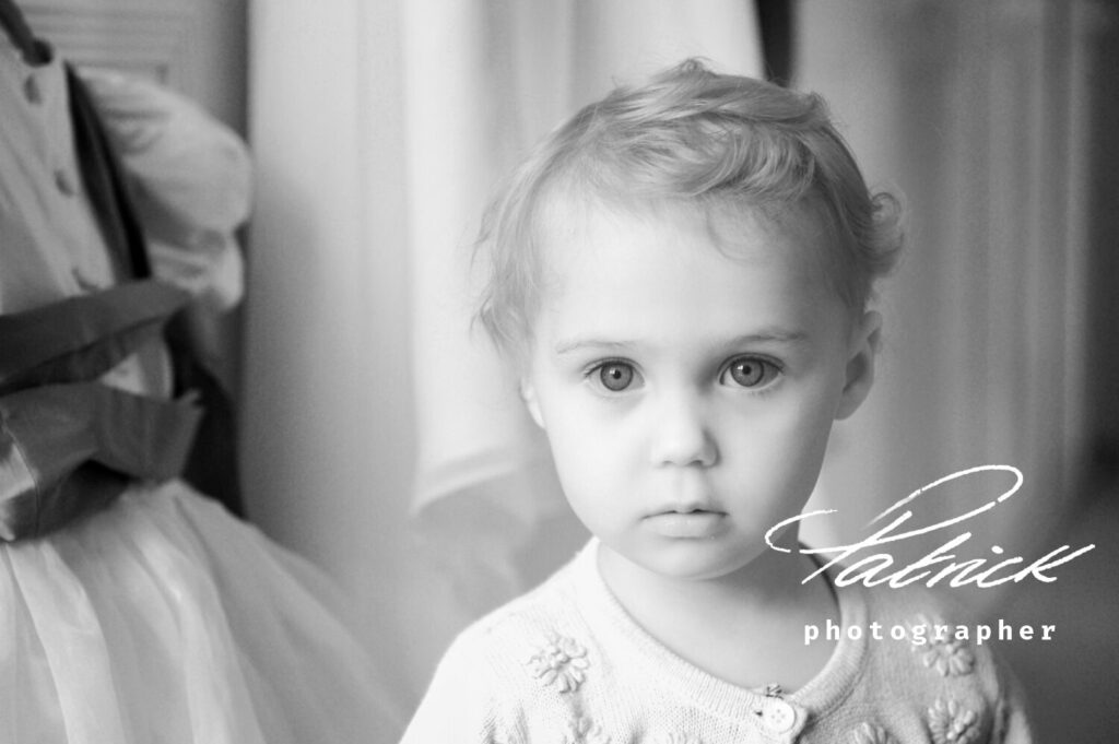 black and white image, young girl, looking directly at camera, bridesmaid dress in background