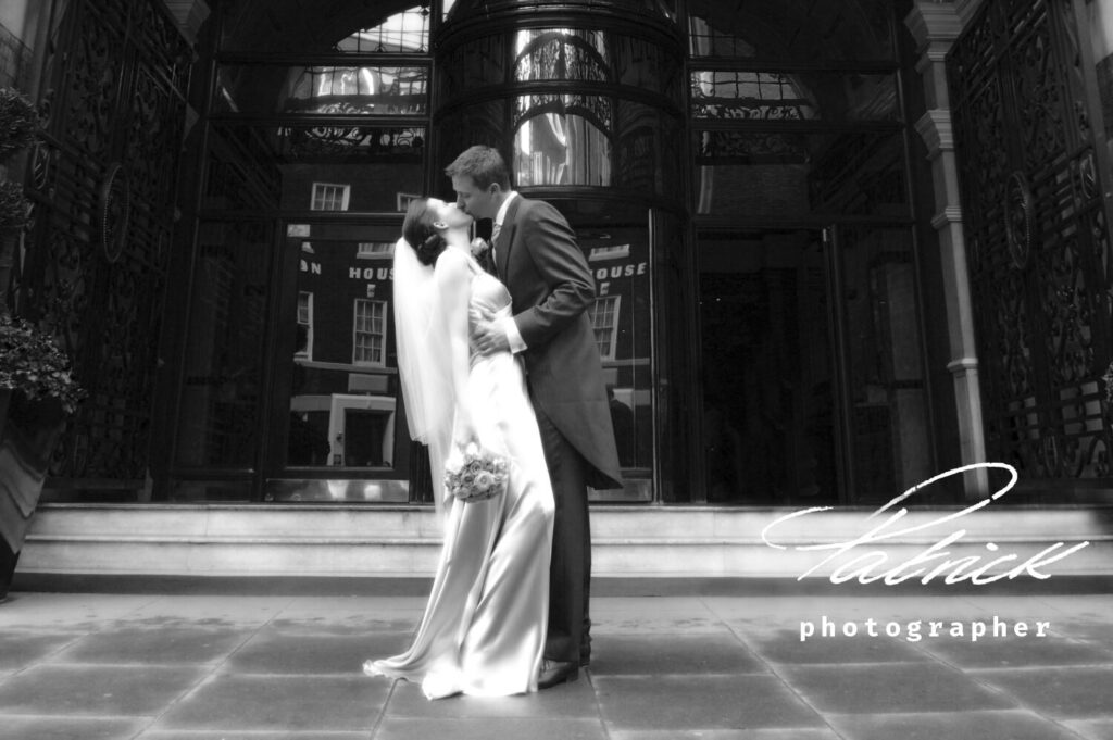 Buckingham gate bride and groom kissing outside revolving doors. silk dress long veil and rose bouquet