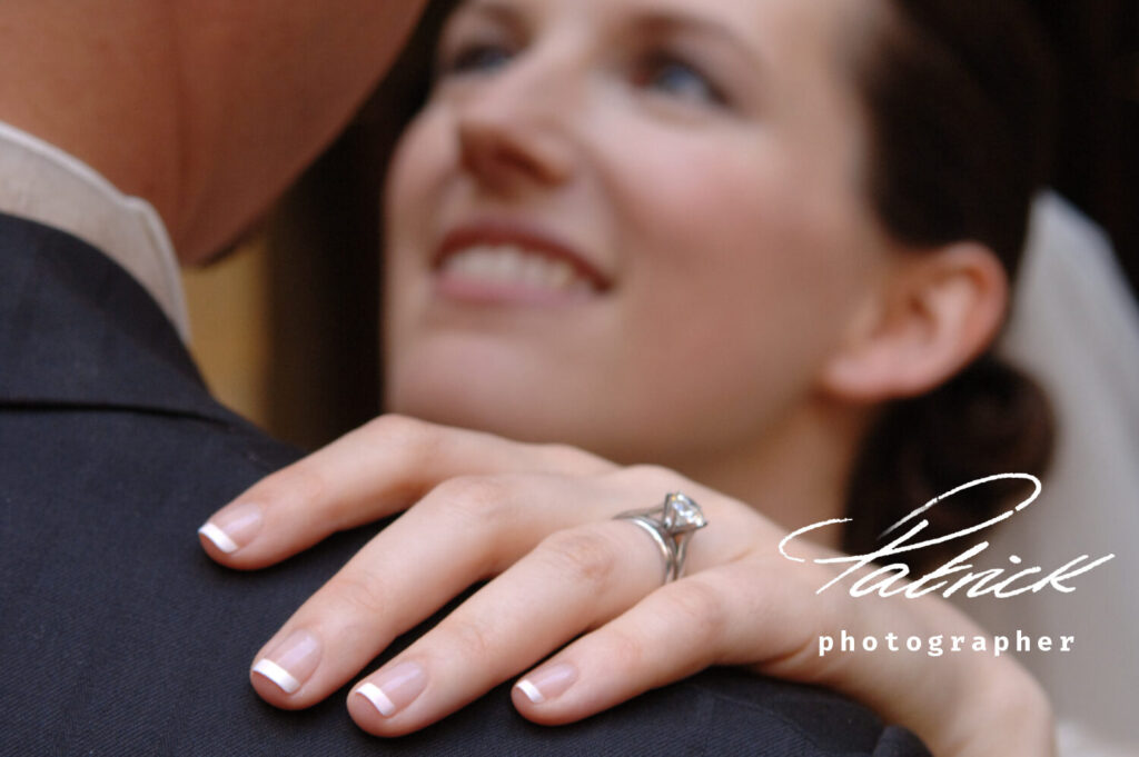 blurred bride looking at groom focus hands and ring on his shoulder