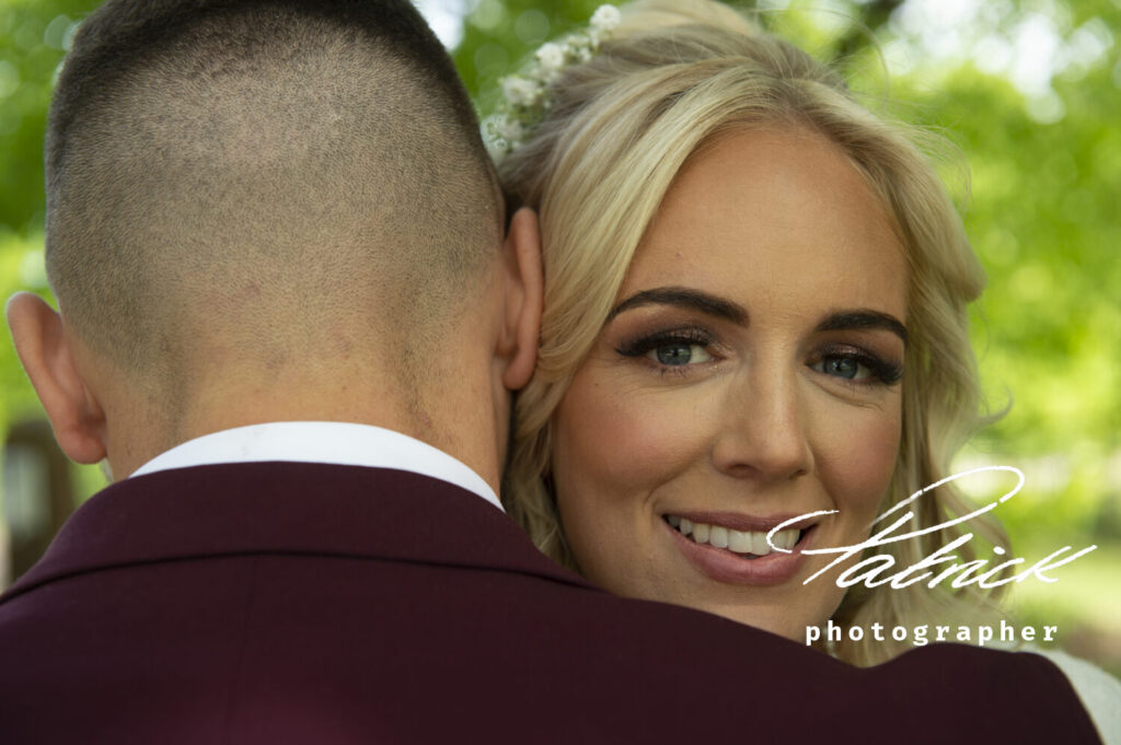 blond bride looking over groom shoulder burgundy jacket