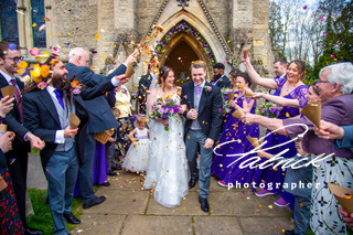 exterior front of church doorway. bride and groom walk towards camera. guests throwing confetti at couple