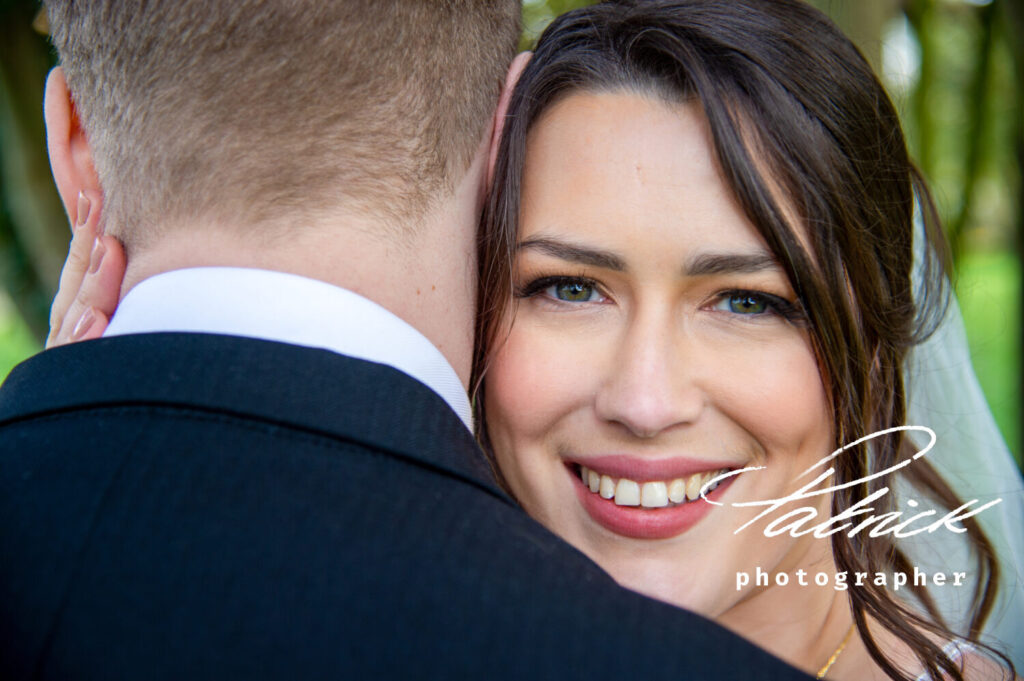 bride looking over grooms shoulder. she is smiling blue eyes pink lipstick brunette