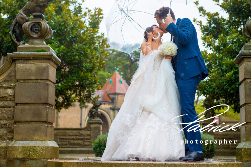 Fanhams Hall, transparent umbrella, bride white dress and veil, white bouquet, groom but suit, outside