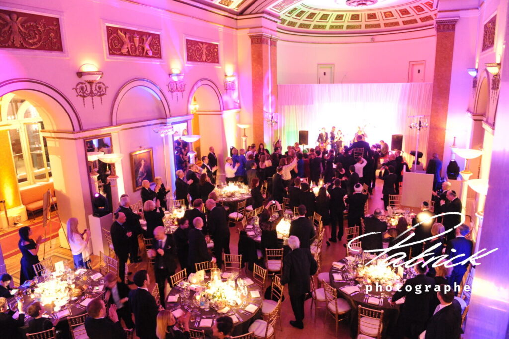 jewish wedding, breakfast, band playing, guests standing around tables, applauding, illuminated building