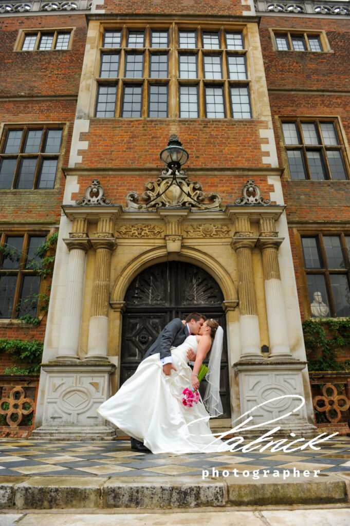 door way, Hatfield House exterior, bride leans back, grooms kissing her. pink and white floral bouquet