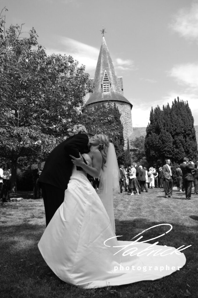 black and white image bride and groom outside church in the grounds with guests in the background