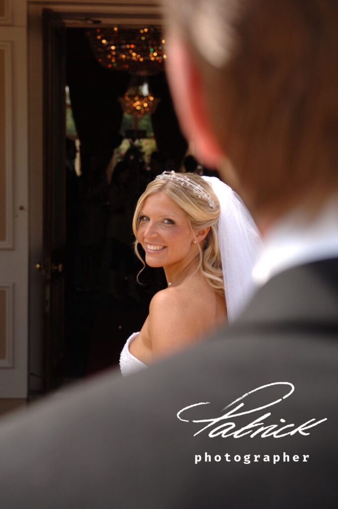 down hall doorway, bride smiles at groom over her left shoulder