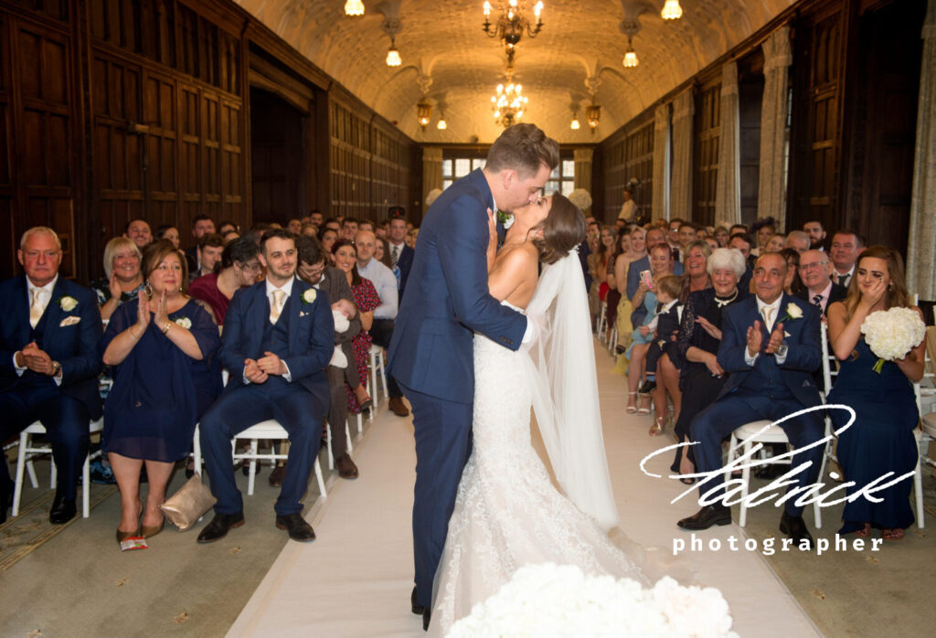 wedding ceremony at fanhams hall, seated guests clap at bride and groom. bride and groom kissing