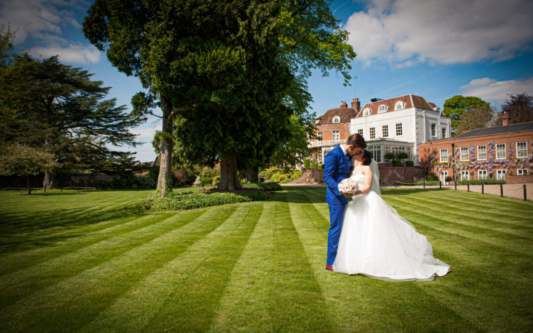 mansion house background, wedding venue, tree foreground, bride and groom embrace, kissing on manicured lawn at St michael's manor