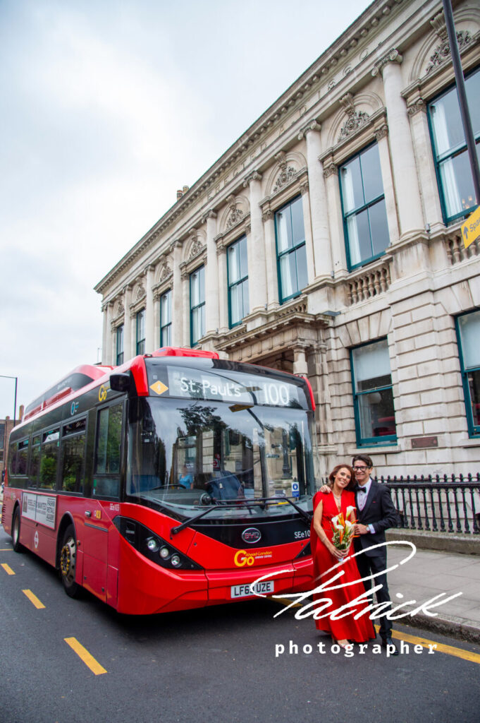 Bride and groom standing in front of single decker city London red bus, red wedding dress, tower hill wedding, bouquet lilies, tower hill registry office