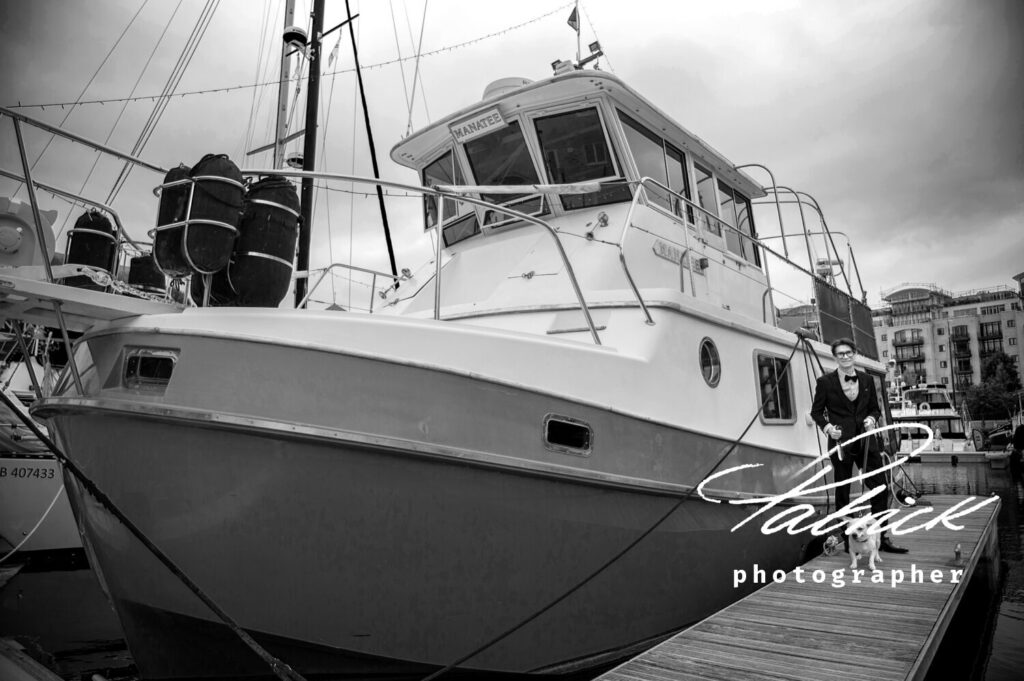 black and white image of groom and his dog standing next to his boat at st katharine docks London