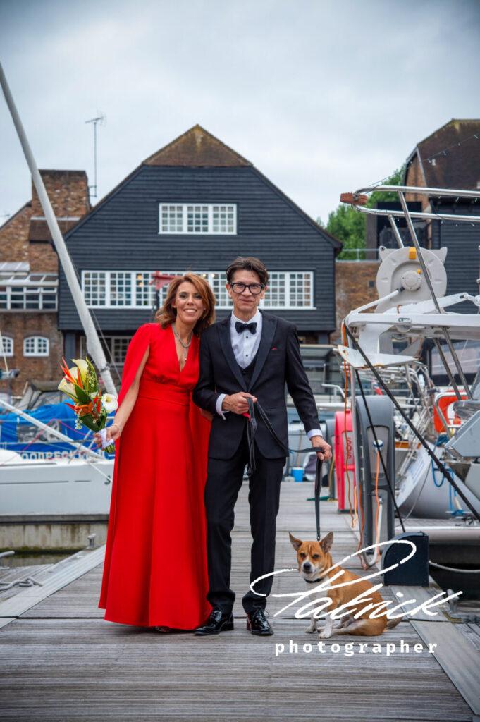 bride and groom and dog at st katharine docks London. bride wears long red dress and groom wears tux