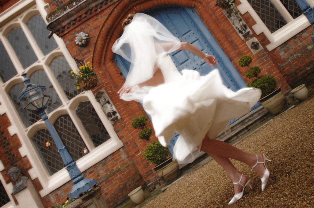 bride gives her dress a dramatic swirl in front of the blue door main entrance of gosfield hall