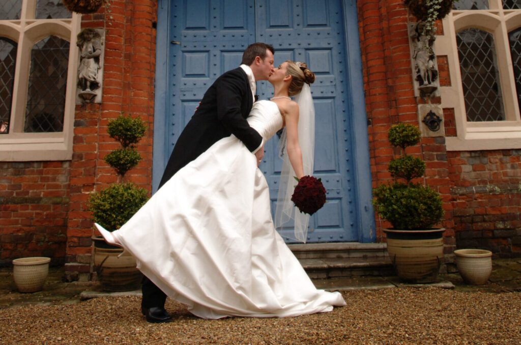 gosfield hall, blue door, groom leans his bride back as he embraces and kisses her,