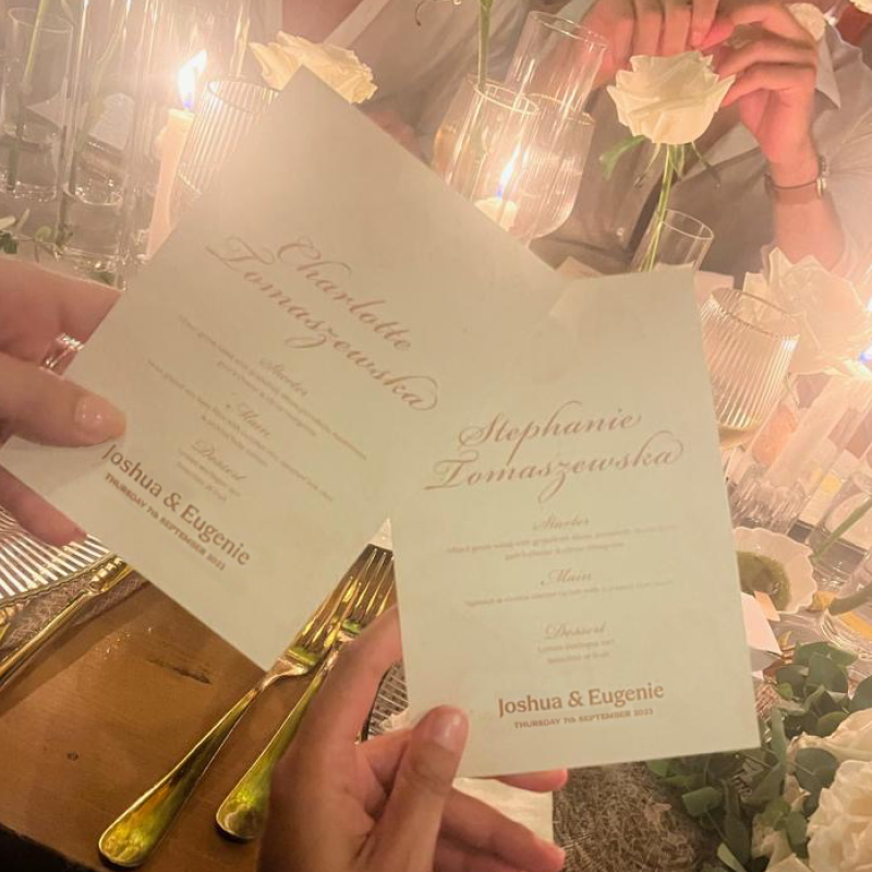 hand showing holding bespoke wedding invitations, dressed tables in background