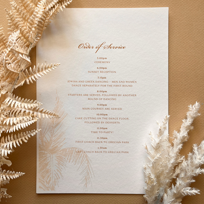 close up of order of service adorned with fern and feathers