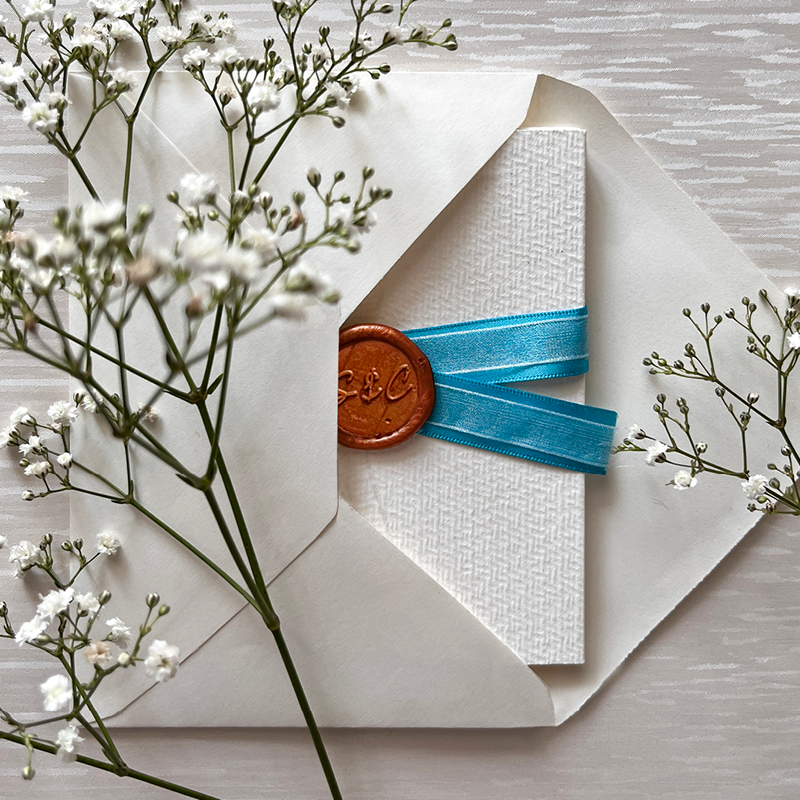 back of enveloped opened exposing invitation showing seal and ribbon. flowers to decorate