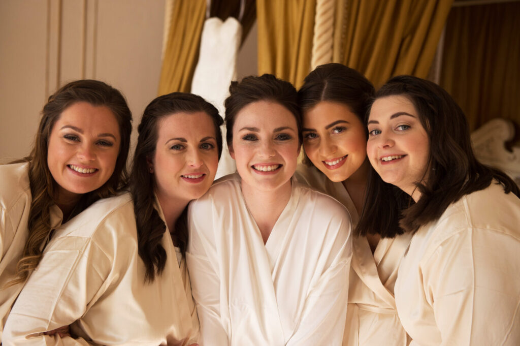 bride surrounded by bridesmaids, close up headshot, getting ready, wearing matching personalised robes, smiling at camera, bridal prep