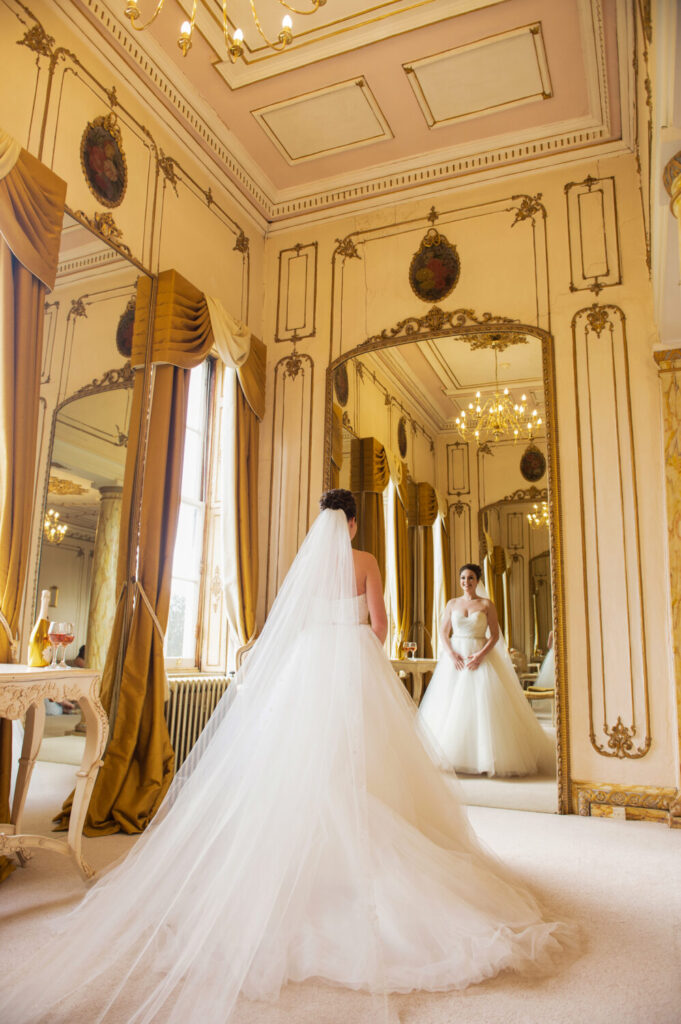 brides gazes at reflection in long full length wall mirror, bridal suite, chandeliers