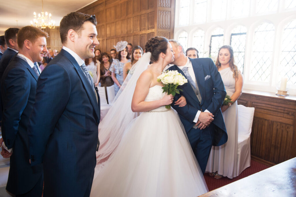 the moment the father of the brides gives his daughter away. he kisses daughter tenderly on her cheek as her husband to be smiles on proudly