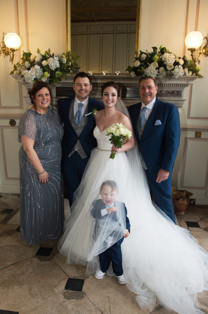 formal group shot parents, bride and groom, page boy hiding under exterior netting of skirt