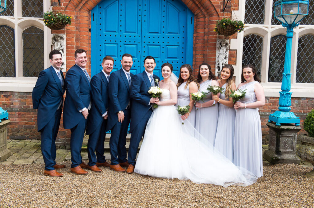 bridal and grooms party gather for a formal group shot outside Gosfield Hall
