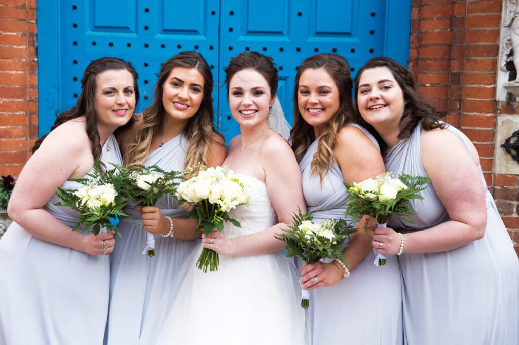 bride and bridesmaids pose with their bouquets, blue door, exterior gosfield hall