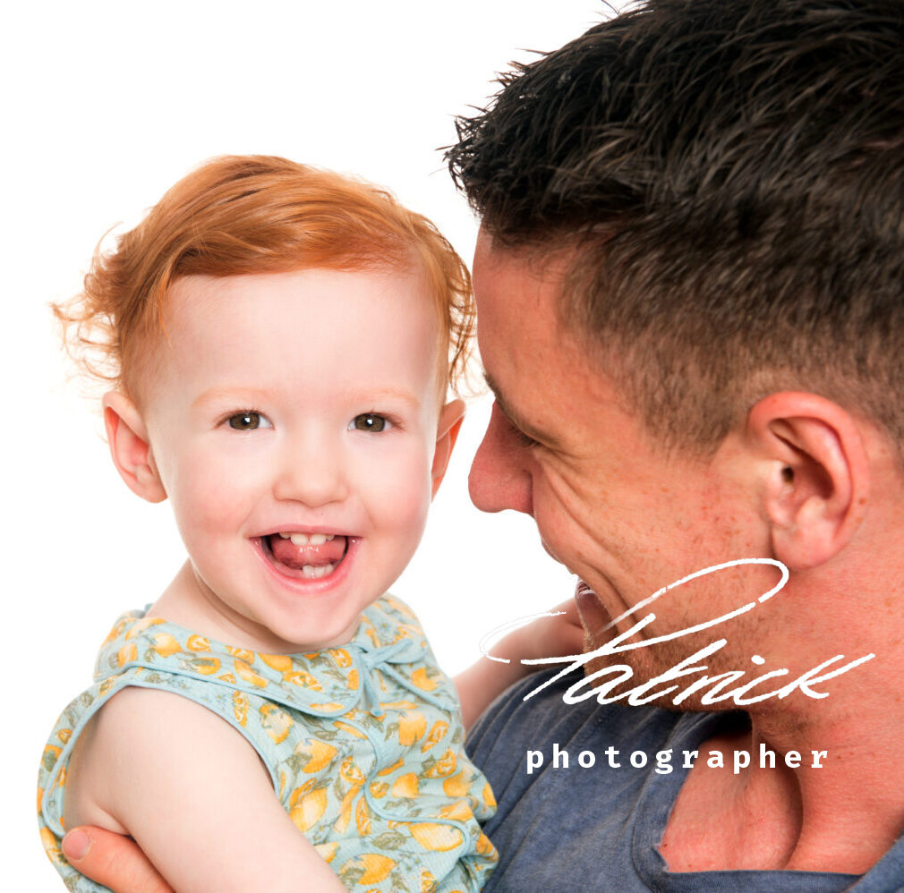 father looking at daughter who is facing camera. studio, portrait, girl green yellow floral dress, red hair, smiling